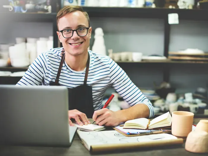 Entrepreneur in striped shirt and apron writes notes beside a laptop and notebooks, representing a local directory